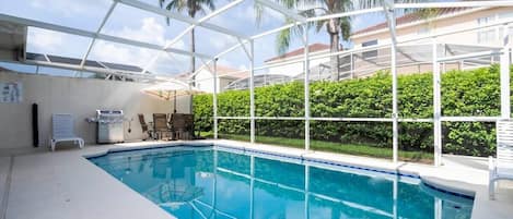 An indoor swimming pool with a glass ceiling, surrounded by greenery and a clear view of palm trees.