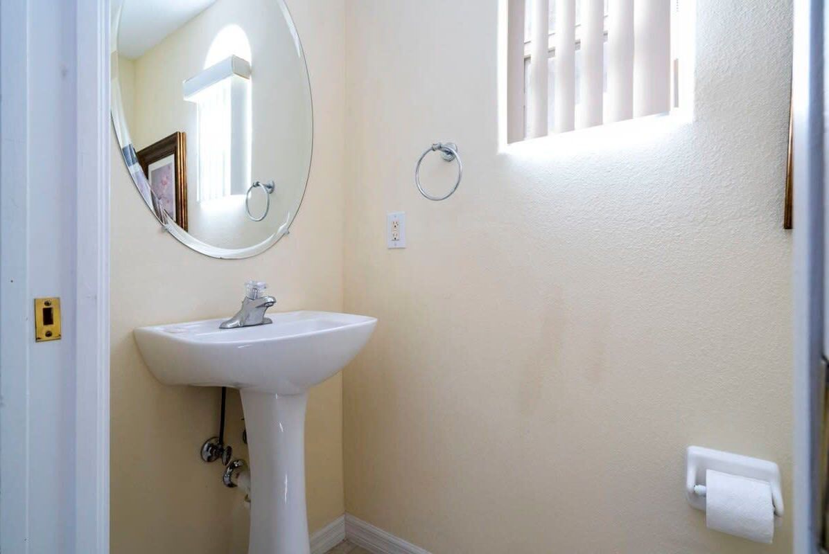 Un bagno con lavandino bianco, uno specchio rotondo, un appendi-asciugamani e una finestra con persiane.