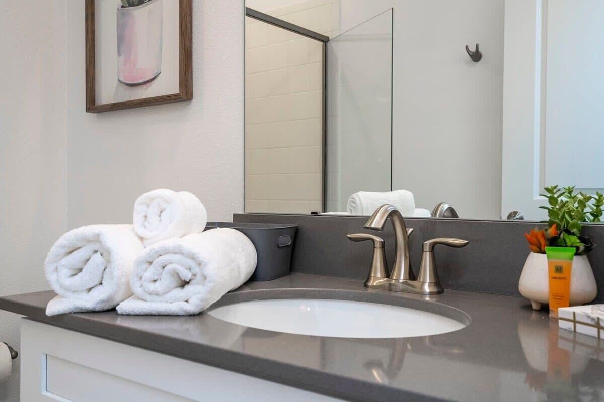 Un baño moderno con un espejo grande, un lavamanos y toallas ordenadamente dobladas en la encimera.