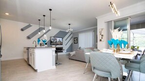 Une cuisine moderne dotée d’un îlot central, de luminaires suspendus et d’un coin repas avec une table et des chaises.