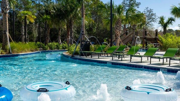 Une piscine avec des bouées gonflables, des chaises longues et une terrasse en bois avec des escaliers.