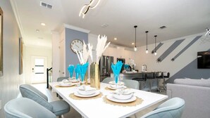 Un espace repas moderne avec une table blanche dressée pour quatre personnes, des chaises bleu clair à revêtement matelassé et des plumes blanches décoratives.