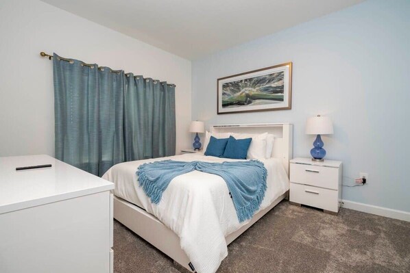 A bedroom with a bed, two bedside tables, a nightstand, a desk, and a painting on the wall.