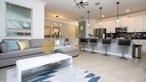 Un salon moderne avec un canapé, une table basse et des tabourets de bar. Il y a également un coin cuisine avec des placards et des appareils électroménagers.