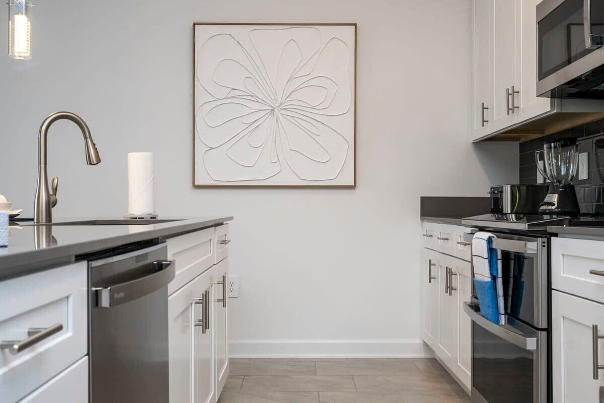 Una cucina moderna con elettrodomestici in acciaio inossidabile, mobili bianchi e un'opera d'arte minimalista a parete.
