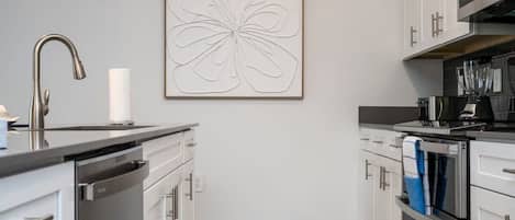 A modern kitchen with stainless steel appliances, white cabinetry, and a minimalist wall art piece.