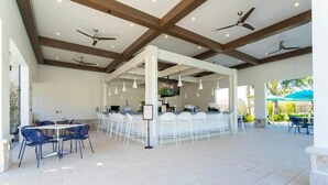 A spacious outdoor dining area with white chairs and tables, ceiling fans, and a bar area with a TV screen. - Marvelous 4Bd with Pool at Storey Lake Resort 2601 (Kissimmee)