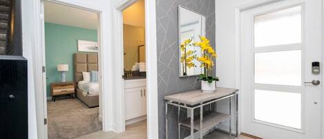 A modern hallway with a grey patterned wall, a white door, and a console table with a vase of yellow flowers.