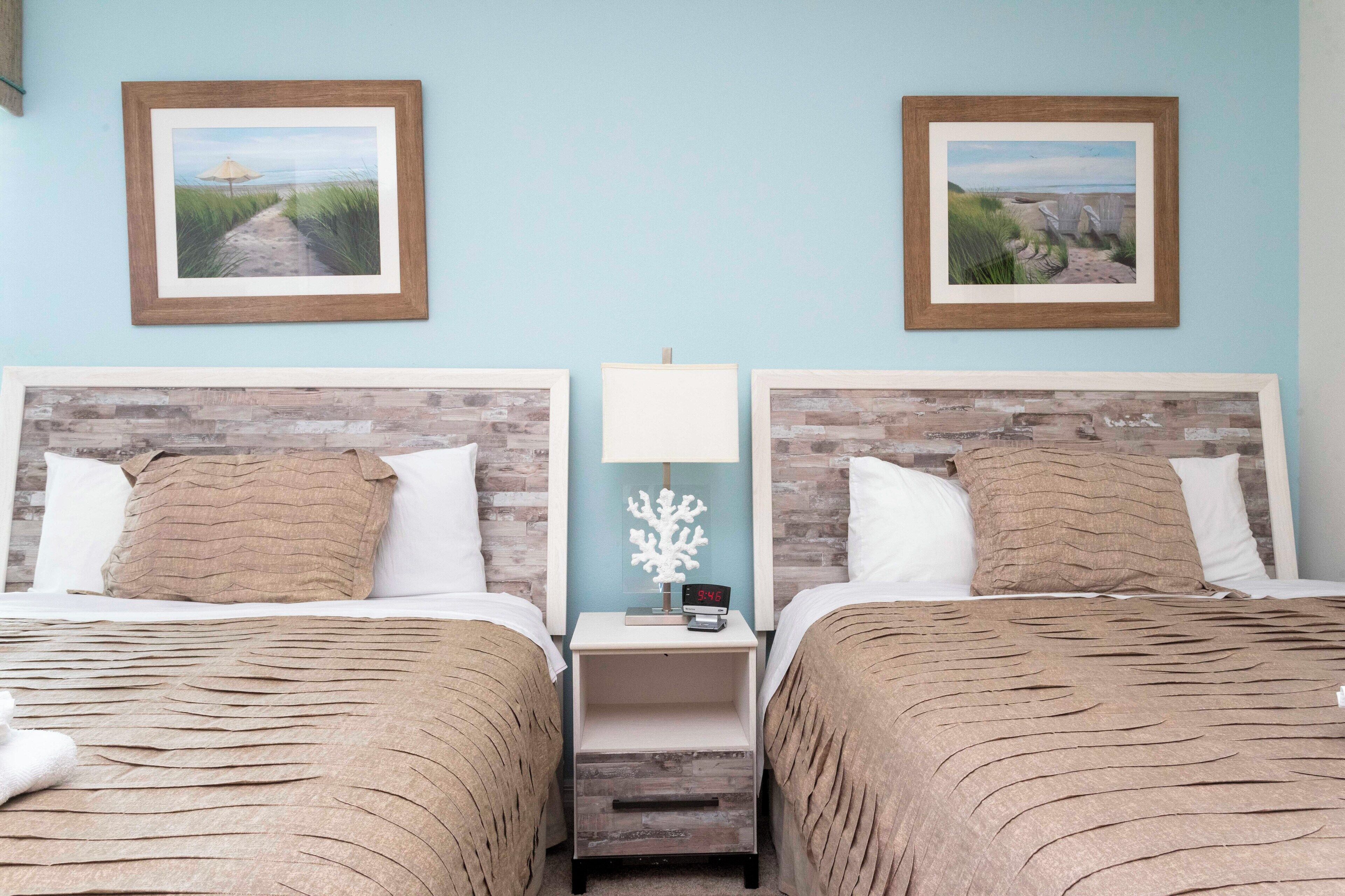 Een hotelkamer met twee bedden, elk met een geborduurde spreideken, een nachtkastje met een lamp en lijstwerken aan de muur.