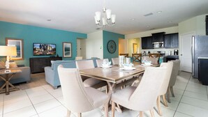 Een moderne woonkamer met een eethoek, keuken, en een grote klok aan de muur.