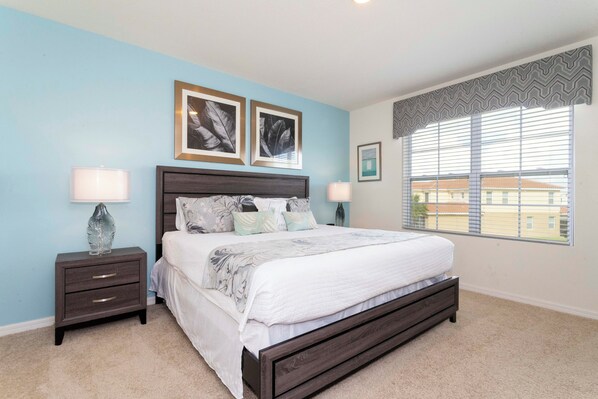 A bedroom with a bed, two nightstands, a window with blinds, and two framed pictures on the wall.