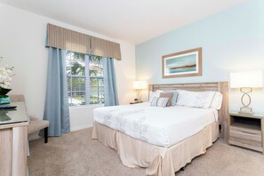 Ein Schlafzimmer mit einem großen Bett, einem Schreibtisch, einem Stuhl, einem Fenster mit Vorhängen und einem Nachttisch mit Lampe.
