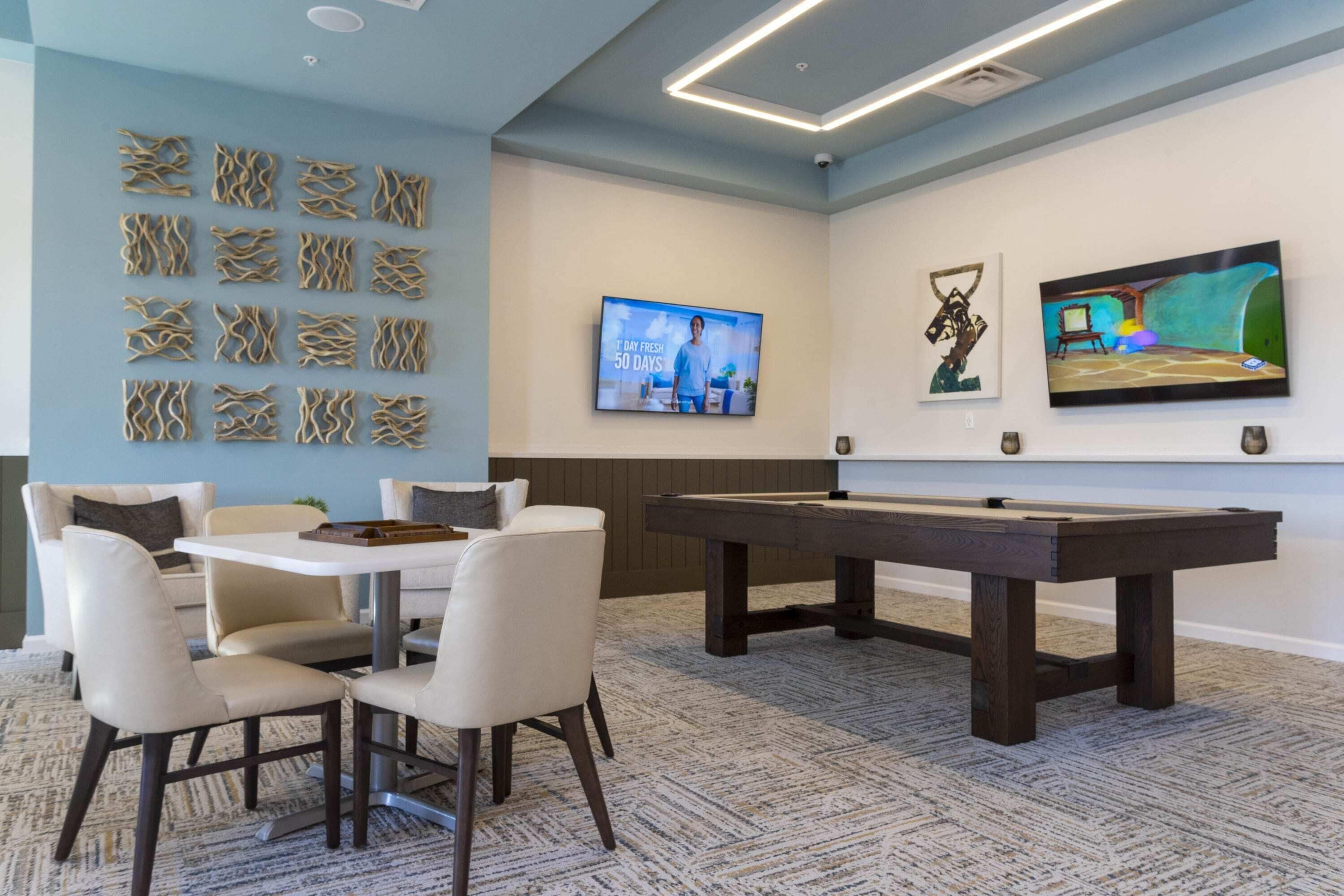 A room with a pool table, a television mounted on the wall, and a seating area with chairs.