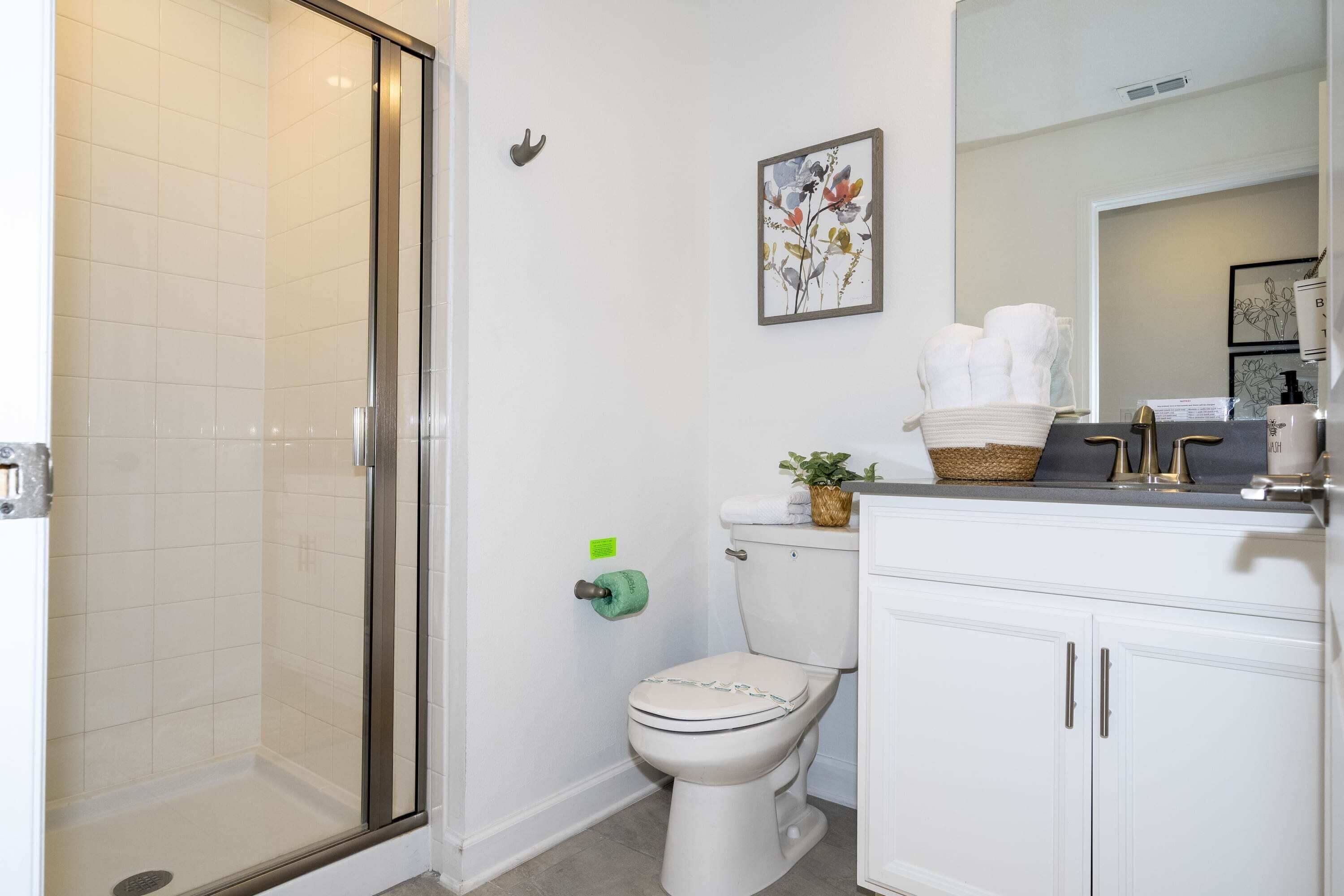 Un baño con cabina de ducha de vidrio, inodoro y tocador blanco con espejo.