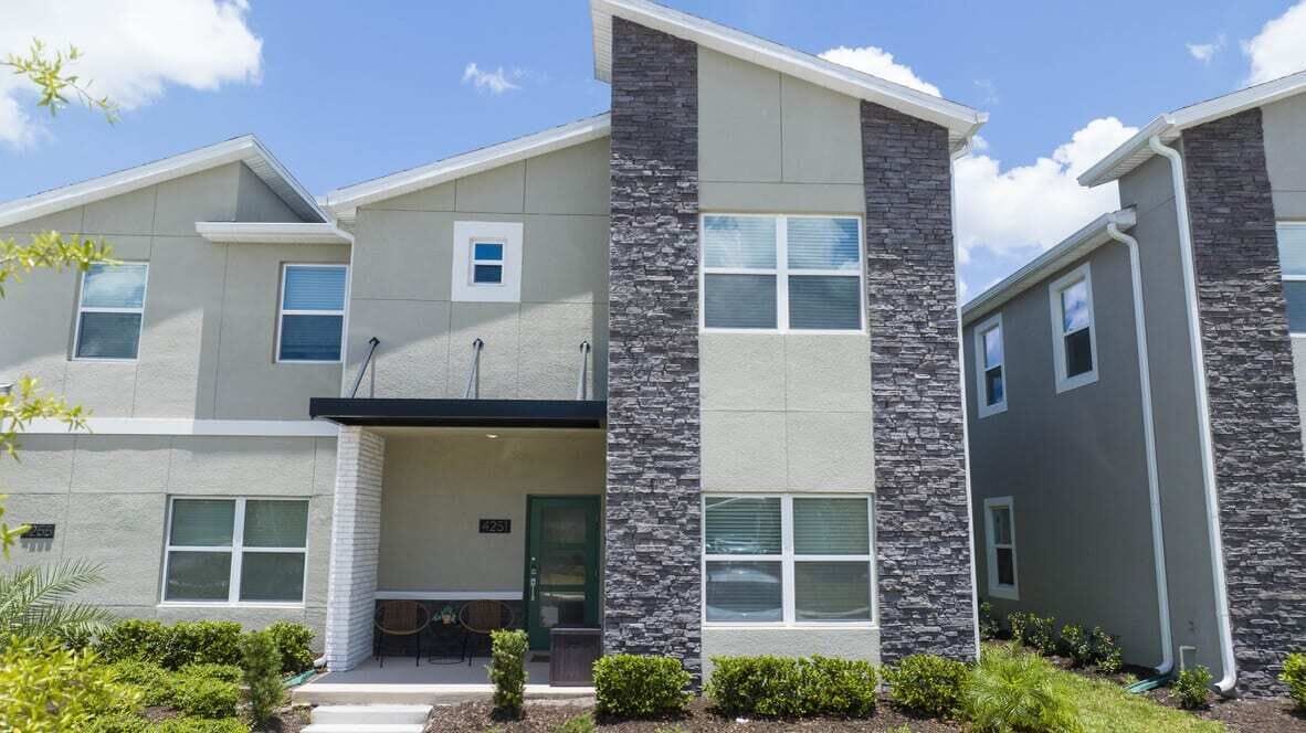 A modern multi-story residential building with a stone facade, multiple windows, and a small porch area.