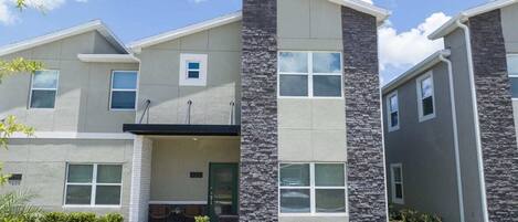 A modern multi-story residential building with a stone facade, multiple windows, and a small porch area.