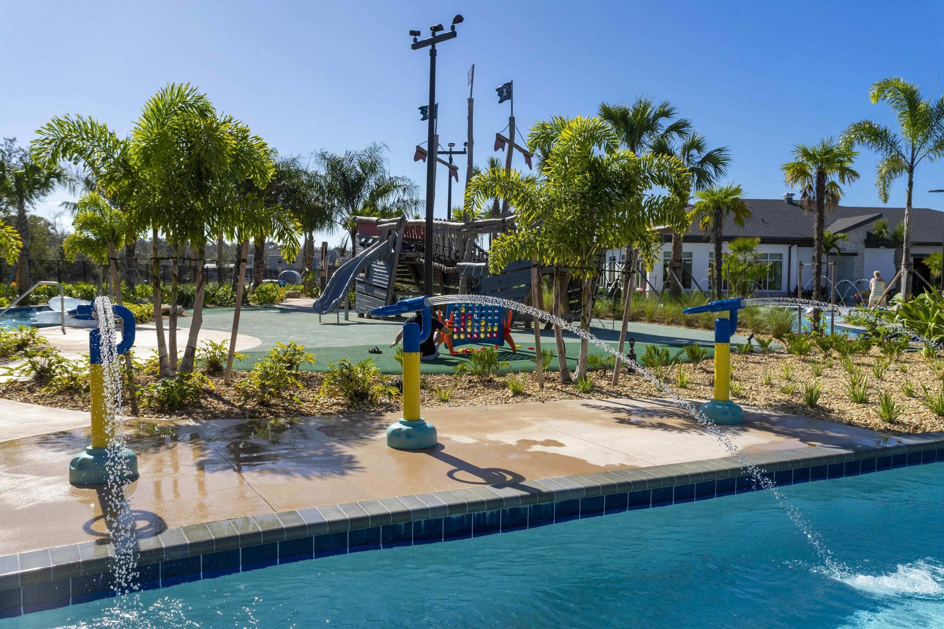 A pool area with a water feature, palm trees, and a playground with slides and a climbing structure.