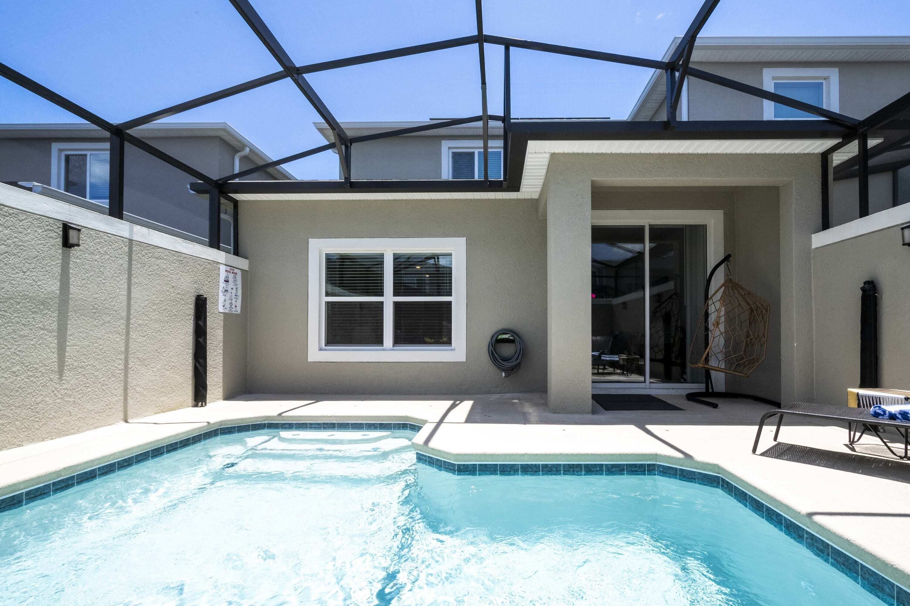 A swimming pool with a glass enclosure, a window, and a door leading to a covered area.