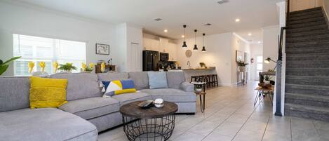 A modern living room with a grey sectional sofa, a round coffee table, and a staircase leading to the upper floor.