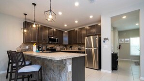 A modern kitchen with dark cabinets, a large island with seating, stainless steel appliances, and pendant lighting. - Stunning 3Bd Close to Disney at Fiesta Key 4764 (Kissimmee)