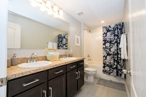 Une salle de bain avec deux lavabos, un grand miroir, une douche avec des rideaux à motifs floraux et des toilettes.