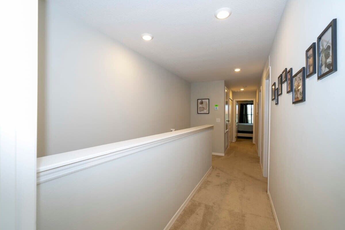 A hallway with a white wainscoting, recessed ceiling lights, and framed pictures on the walls.