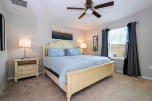 Une chambre à coucher comprenant un lit, des tables de chevet, un ventilateur de plafond et une fenêtre avec des rideaux.