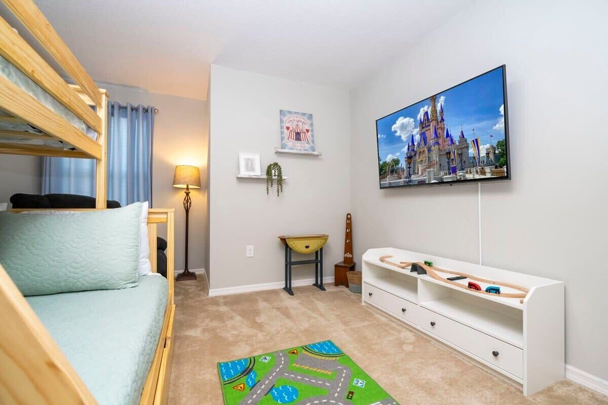 A child's room with bunk beds, a TV, a play mat, and a castle-themed picture.