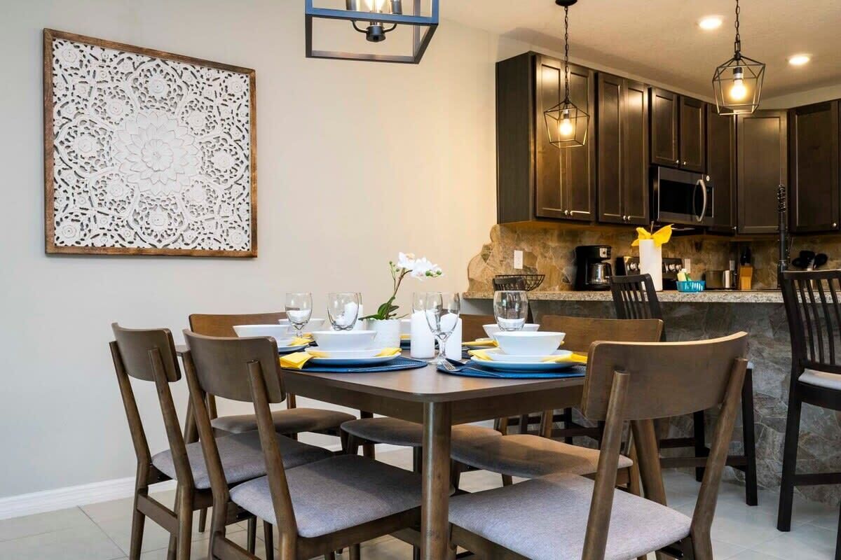 A dining area with a table set for four, surrounded by chairs. A decorative wall piece is above the table.