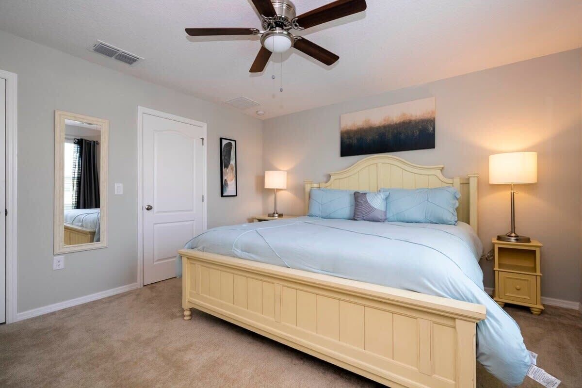 A bedroom with a bed, two bedside tables, a ceiling fan, a door, and a painting on the wall.