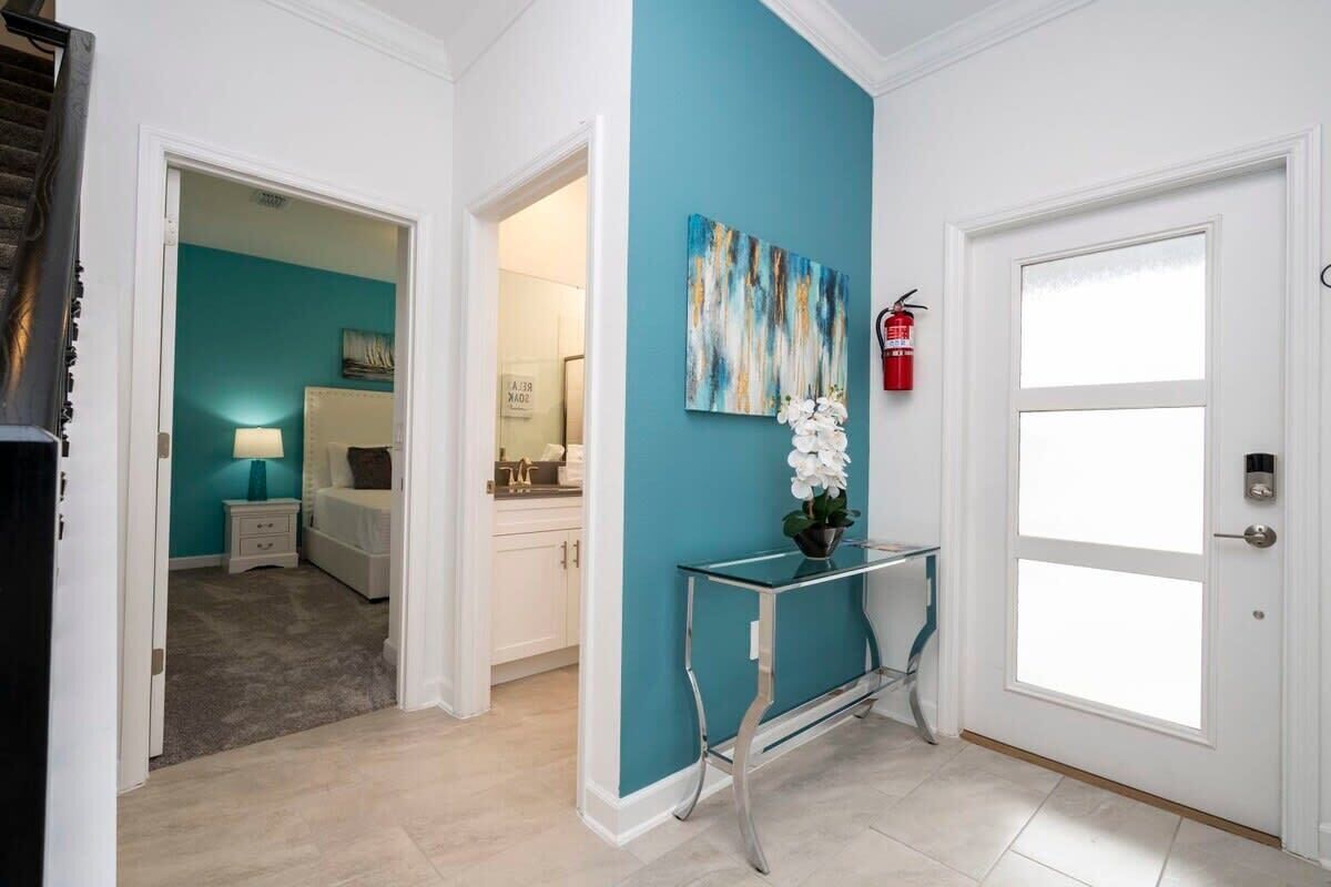 Un couloir avec un mur de couleur turquoise, une porte blanche et une console en verre sur laquelle est posée une orchidée blanche.