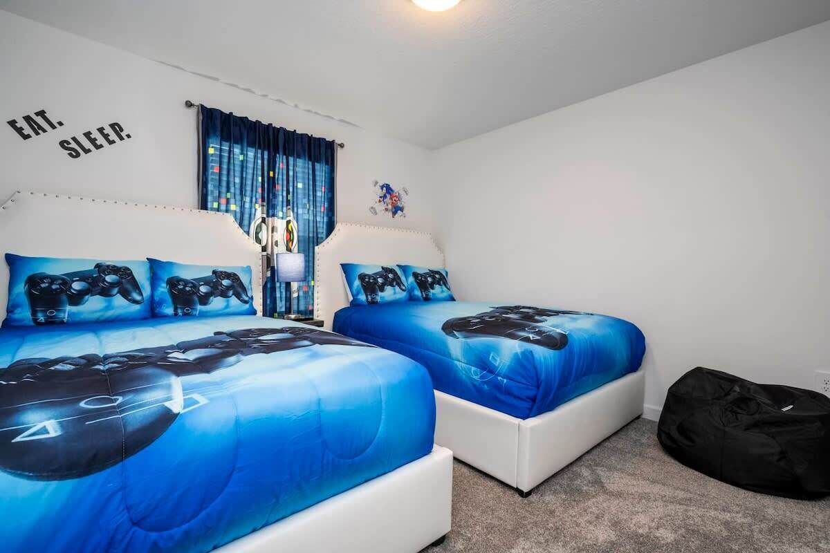 A bedroom with two beds, each with blue bedding featuring a video game controller design.