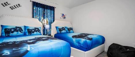 A bedroom with two beds, each with blue bedding featuring a video game controller design.