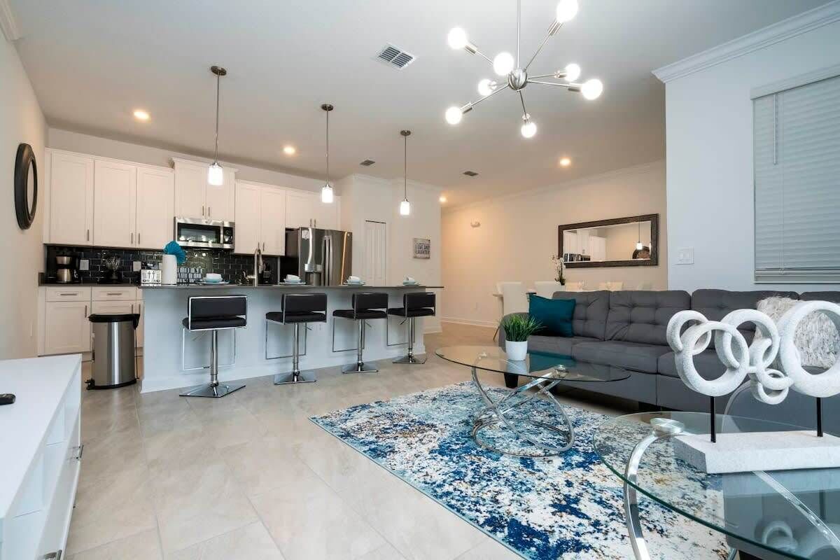 A modern kitchen with white cabinets, a stainless steel refrigerator, and a bar area with stools.