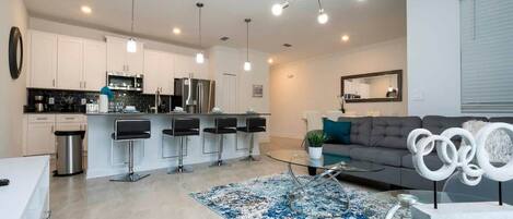 A modern kitchen with white cabinets, a stainless steel refrigerator, and a bar area with stools.