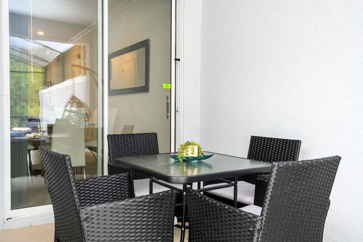 Una puerta de cristal da acceso a un comedor con una mesa y cuatro sillas de mimbre.