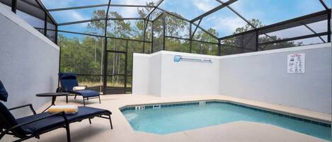 An indoor swimming pool with clear glass walls, blue lounge chairs, and a pool ladder.