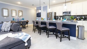 A modern kitchen with a central island, bar stools, and a dining area with a sofa and chairs. - Stunning 4 Bd w/ Pool Close to Disney at Champions Gate 1158 (Davenport)