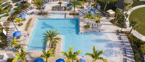 Una gran piscina rodeada de sillones de descanso y sombrillas, con palmeras y un campo de golf al fondo.