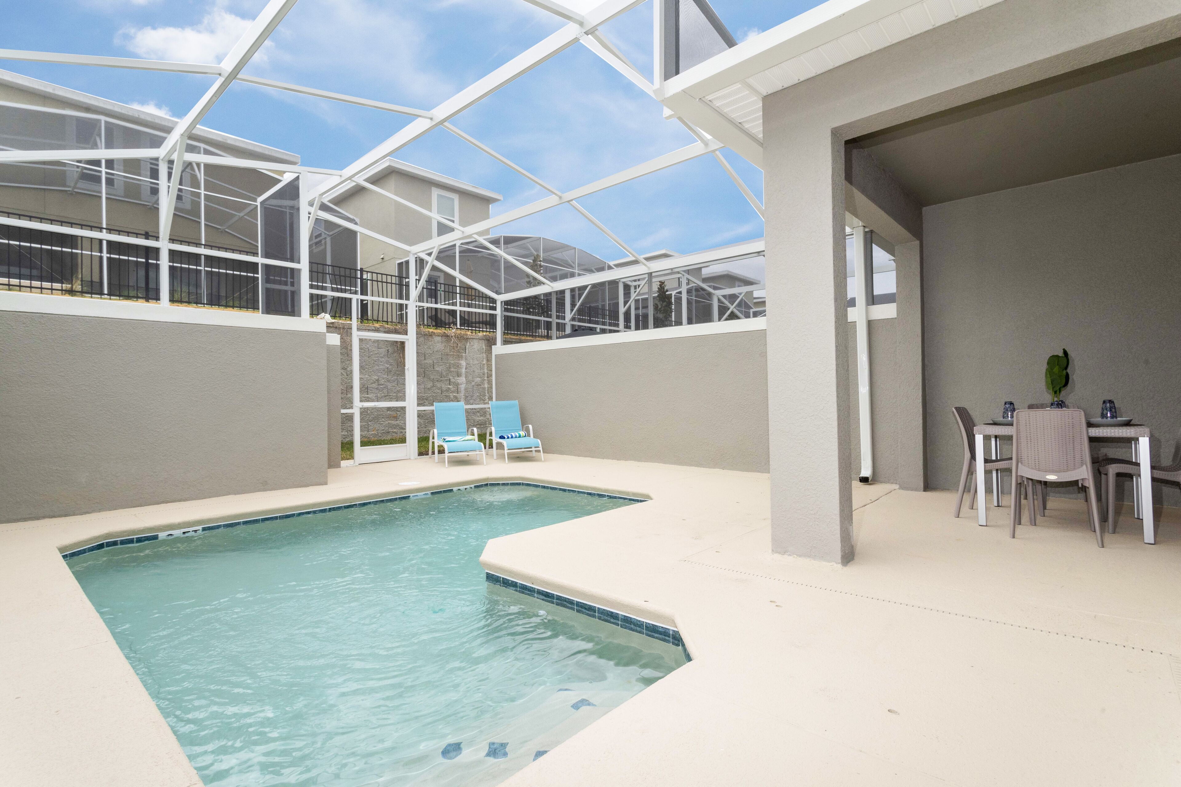 An indoor swimming pool with a glass ceiling, lounge chairs, and a table with chairs.