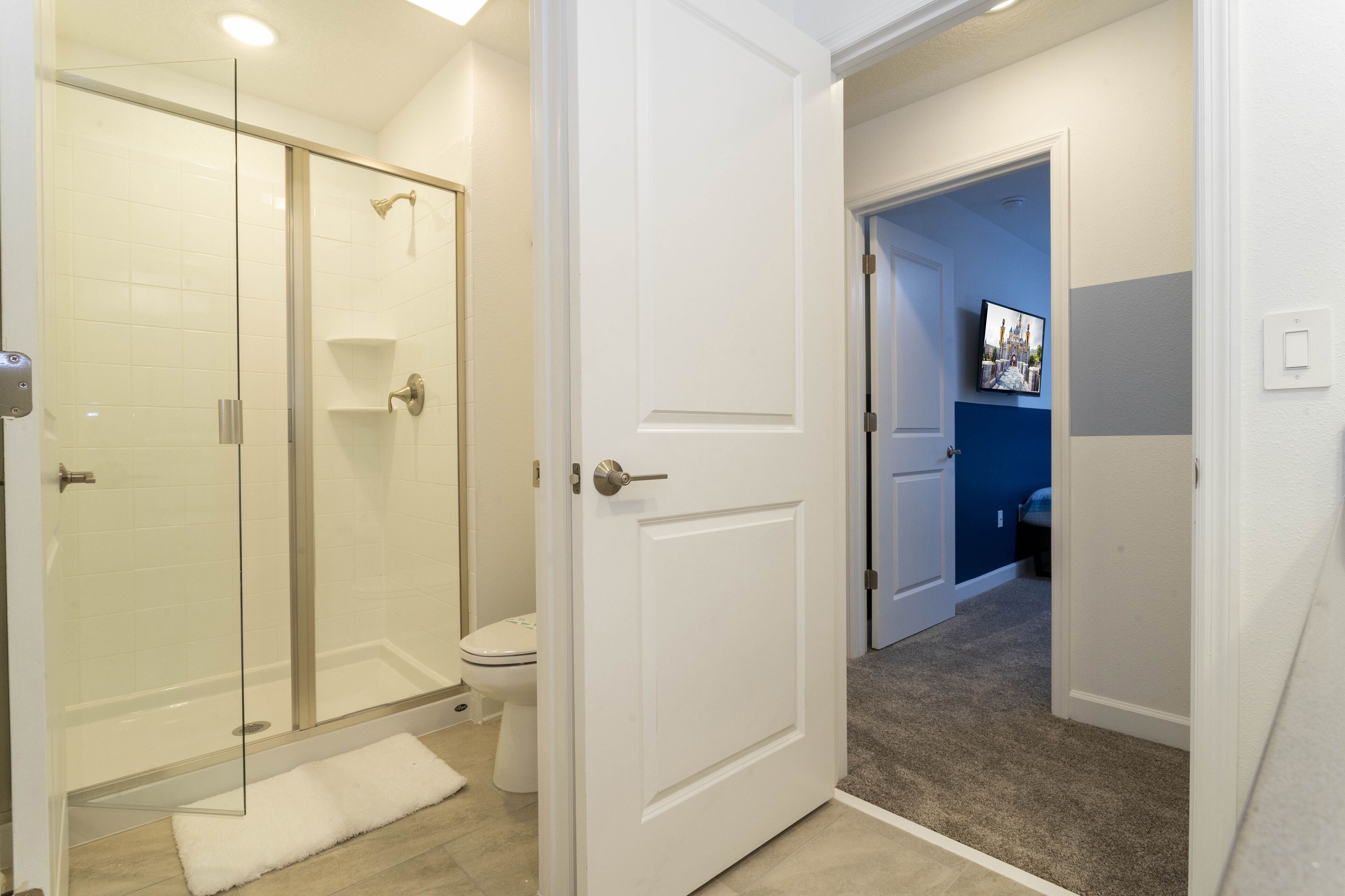 A bathroom with a glass shower enclosure, a toilet, and a white door leading to another room.