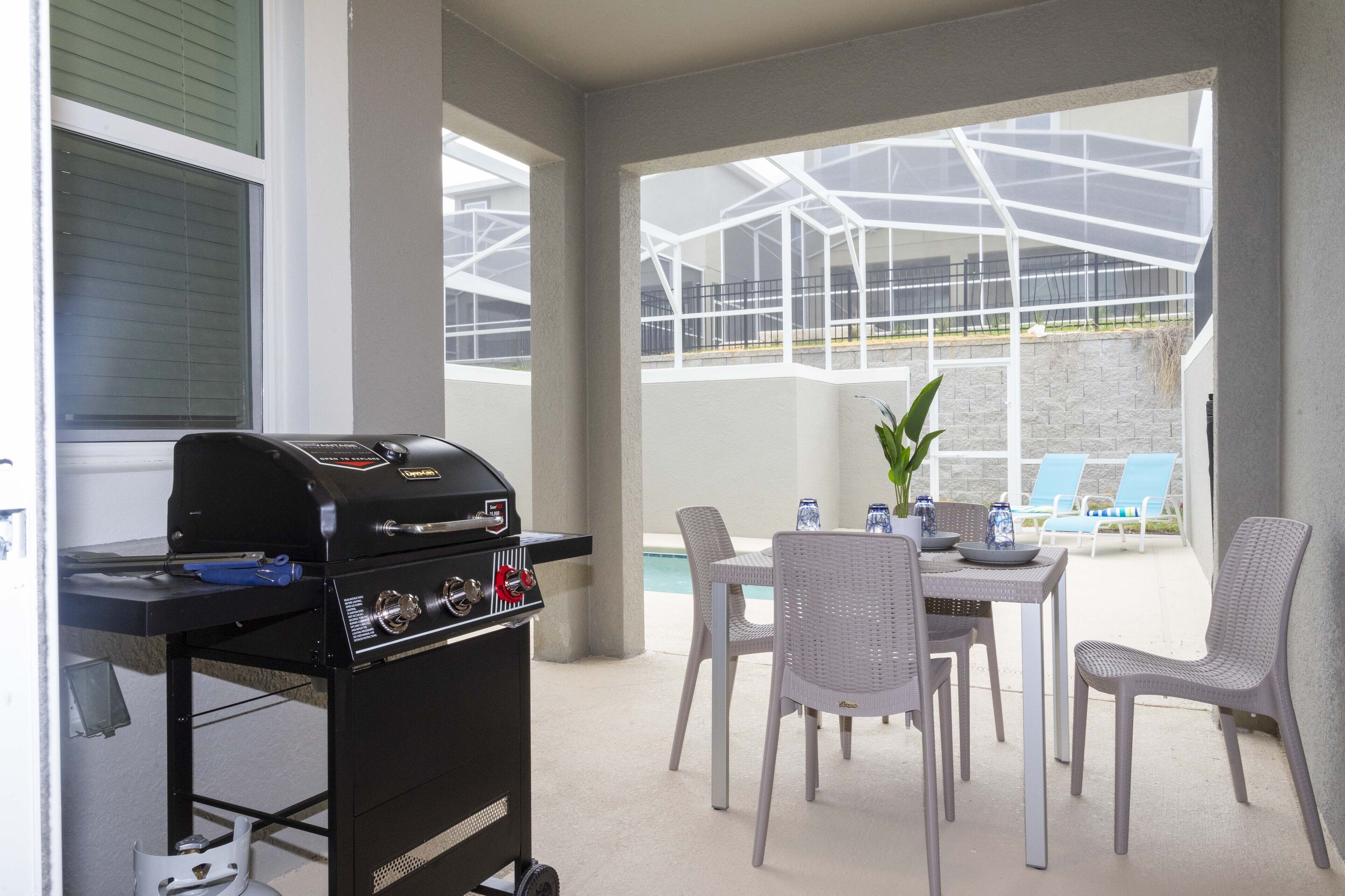 Une terrasse extérieure équipée d’un barbecue, d’une table à manger, de chaises et offrant une vue sur une piscine et un espace de détente.