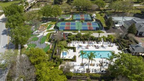 An aerial view of a resort with multiple tennis courts, a swimming pool, and lounge areas. - Stunning 5 Bd Home w/ Pool Close to Disney 7420 (Kissimmee)