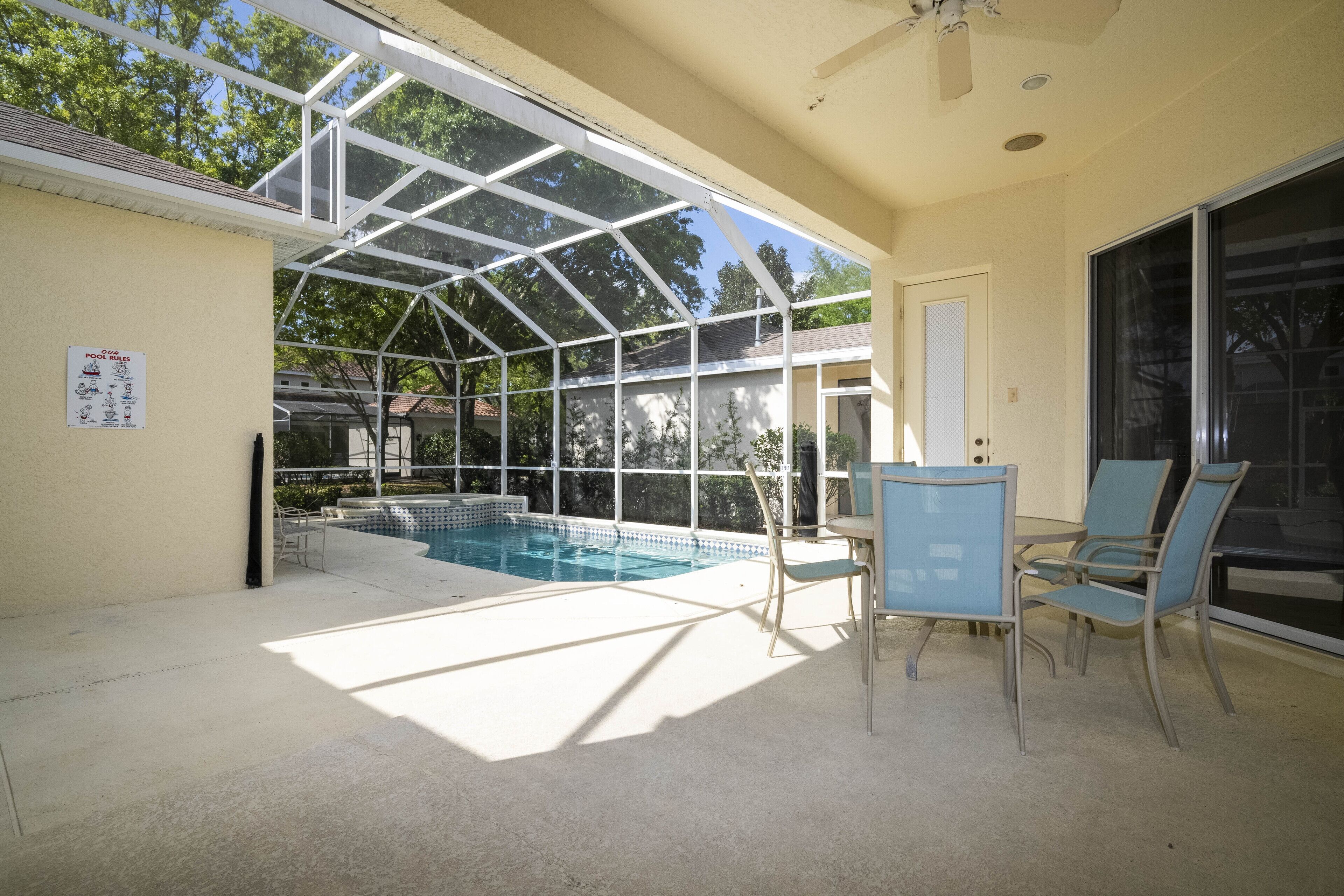 A covered outdoor swimming pool with a glass enclosure, a table, and chairs.