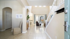 A spacious hallway with a dining area, a staircase, and a door with a security lock. - Stunning 5 Bd Home w/ Pool Close to Disney 7420 (Kissimmee)