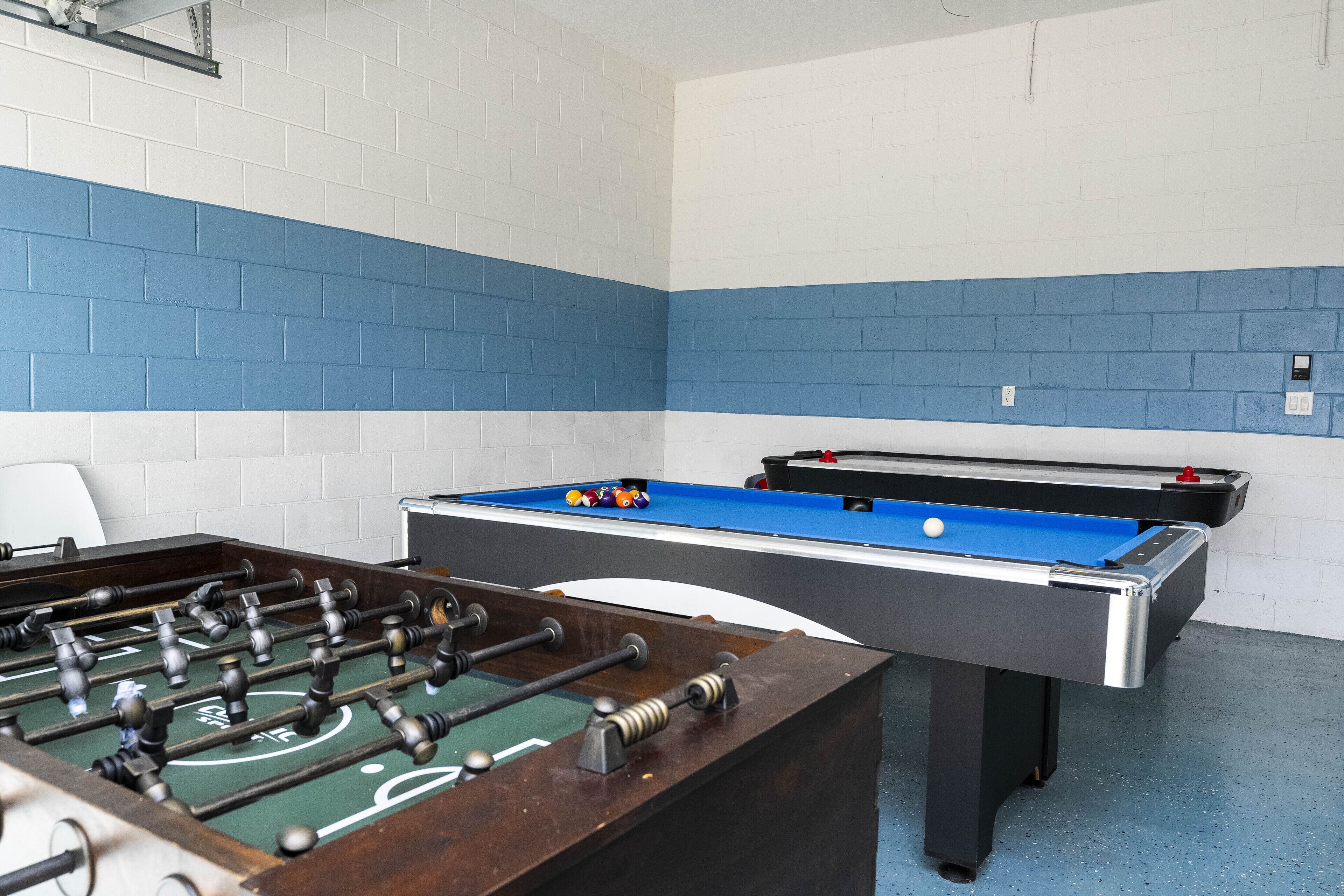 A room with a foosball table and a pool table, both with blue and white walls.