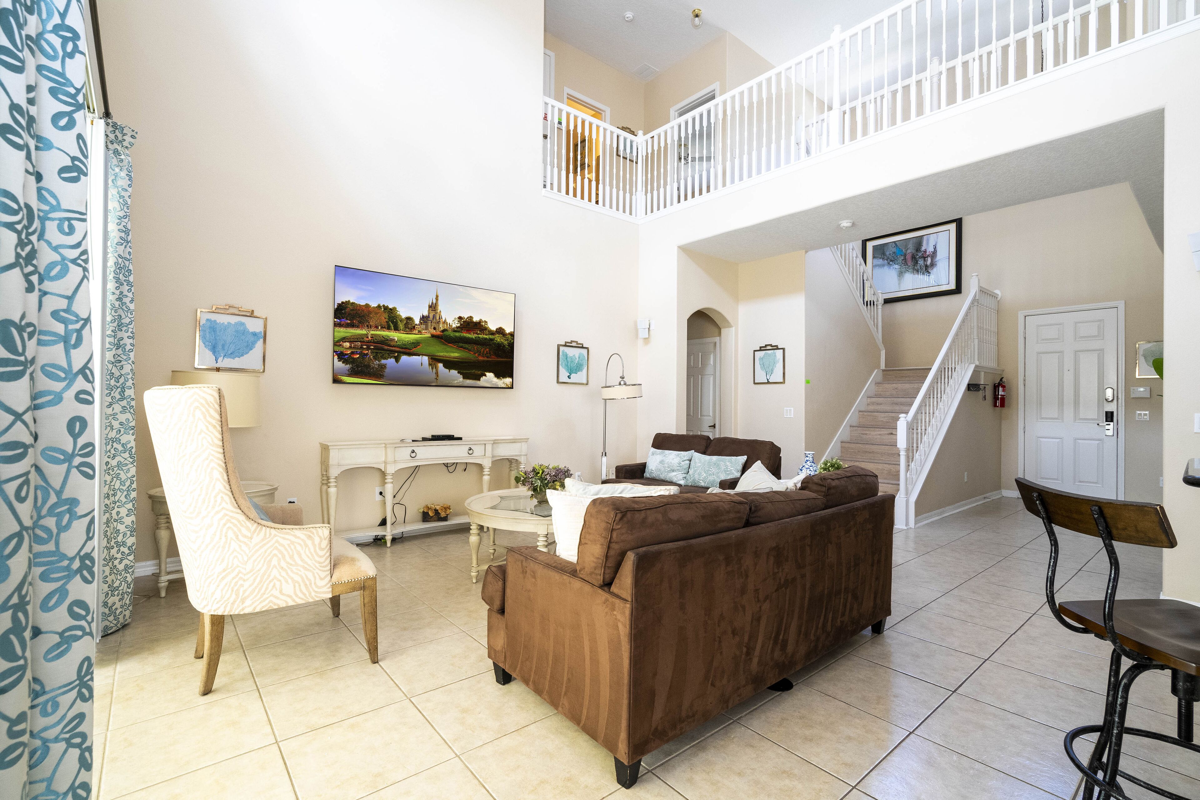 Un vaste espace de vie comprenant un canapé marron, un fauteuil blanc et une table à manger. Un escalier mène à l’étage supérieur.