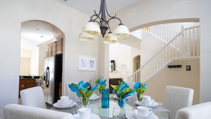 A dining area with a glass table, white chairs, and a chandelier. - Stunning 5 Bd Home w/ Pool Close to Disney 7420 (Kissimmee)