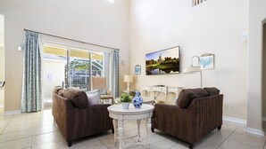 A living room with two brown sofas, a white round table, and a large window with curtains. - Stunning 5 Bd Home w/ Pool Close to Disney 7420 (Kissimmee)