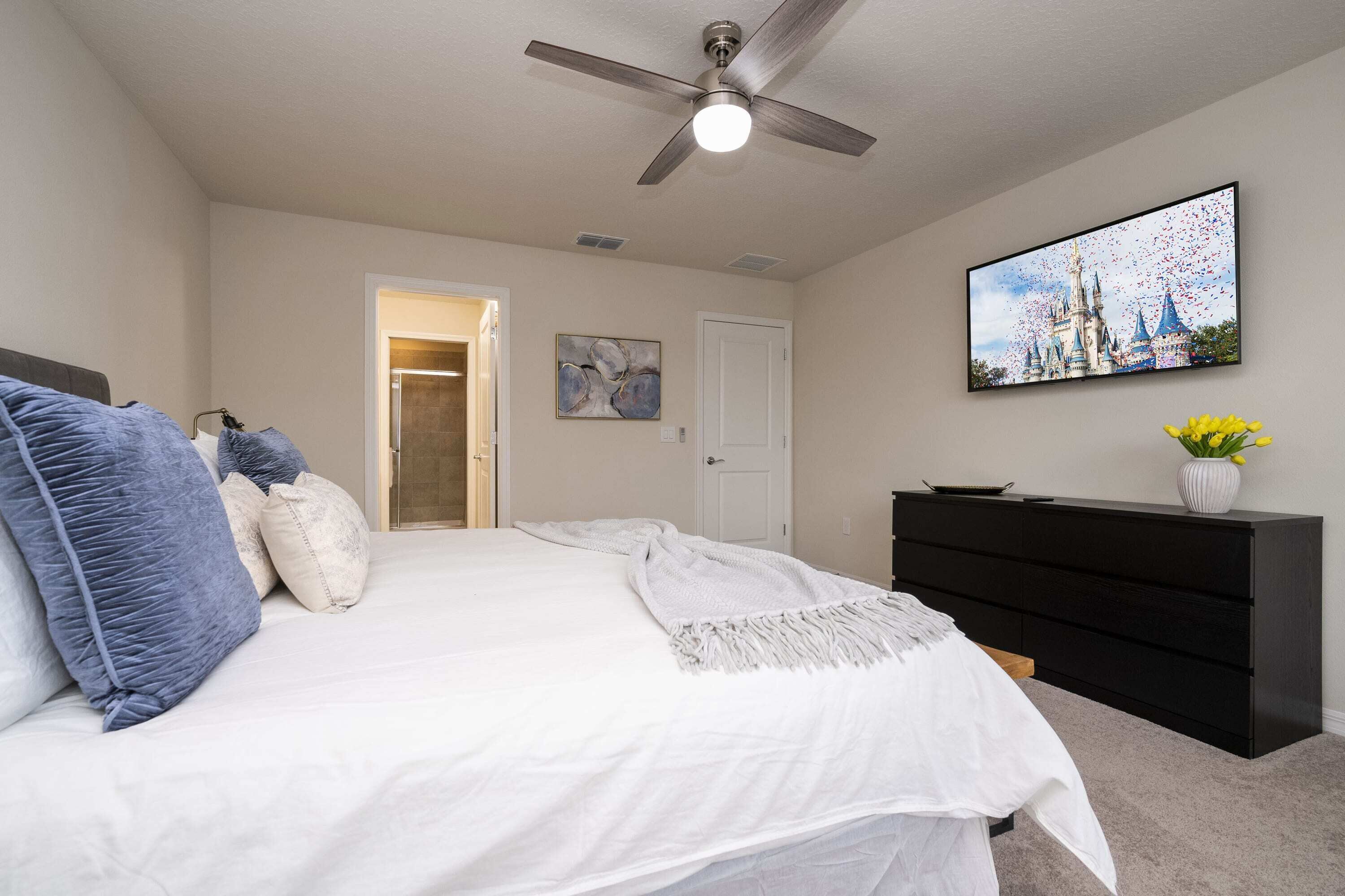 A bedroom with a bed, a ceiling fan, a TV, a dresser, and a painting on the wall.